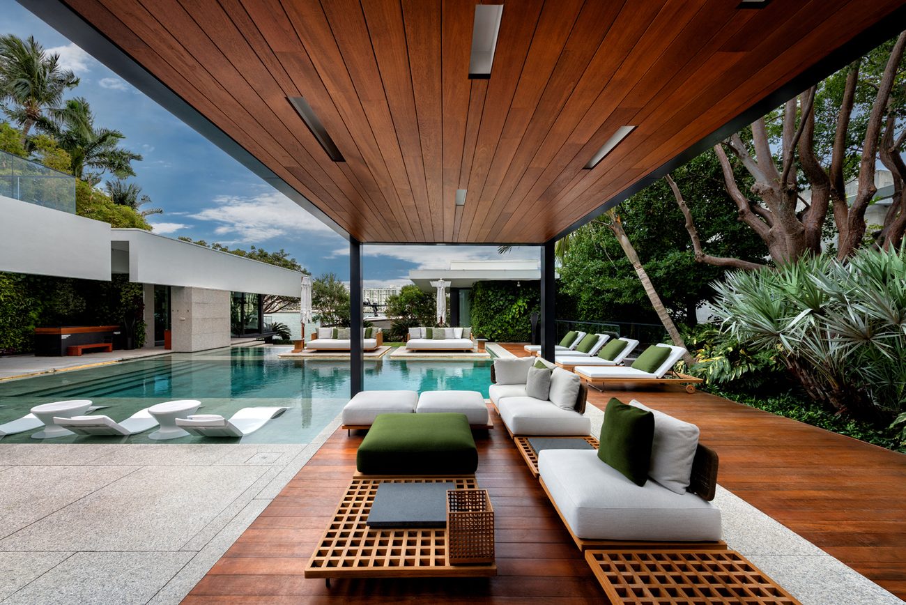 Covered terrace with a wood ceiling and lounge seating beside a renovated pool