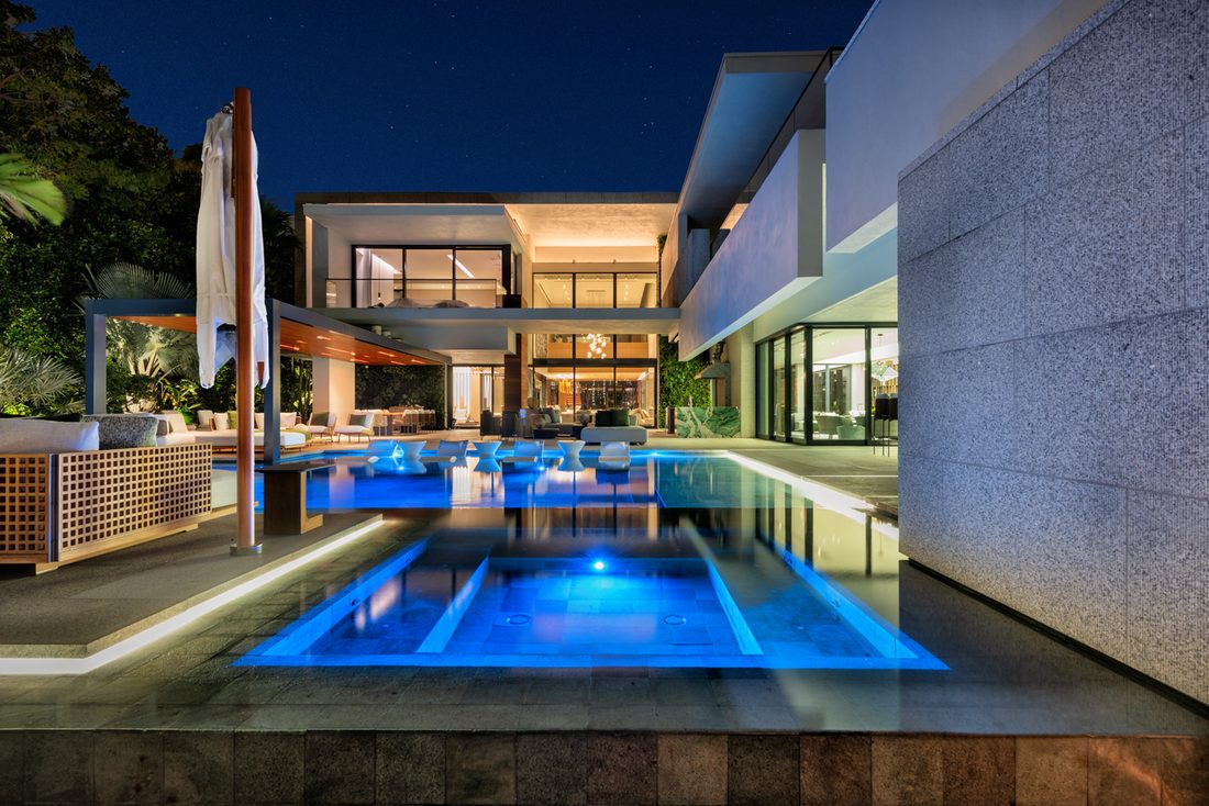Renovated pool glowing blue at night beside the home